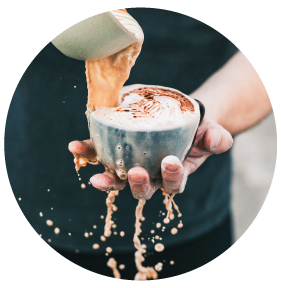 Mann schüttet Kaffee von einer Tasse in die andere, diese läuft dabei über